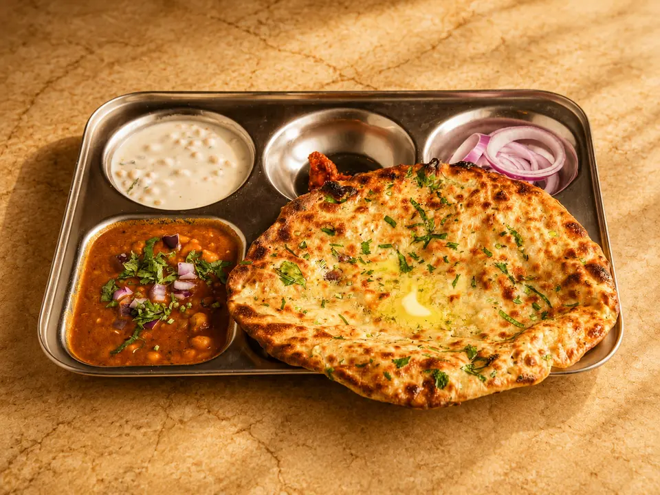 Amritsari kulcha thali: a stuffed kulcha with chana masala, raita, onions and butter on a steel tray